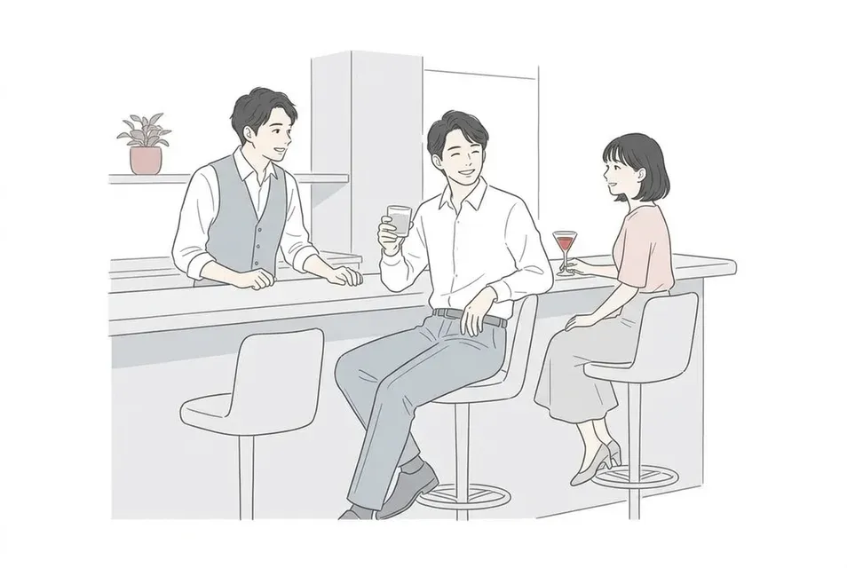 出張先の落ち着いたバーのカウンターで、バーテンダーや隣の客と和やかに会話を楽しむ様子。