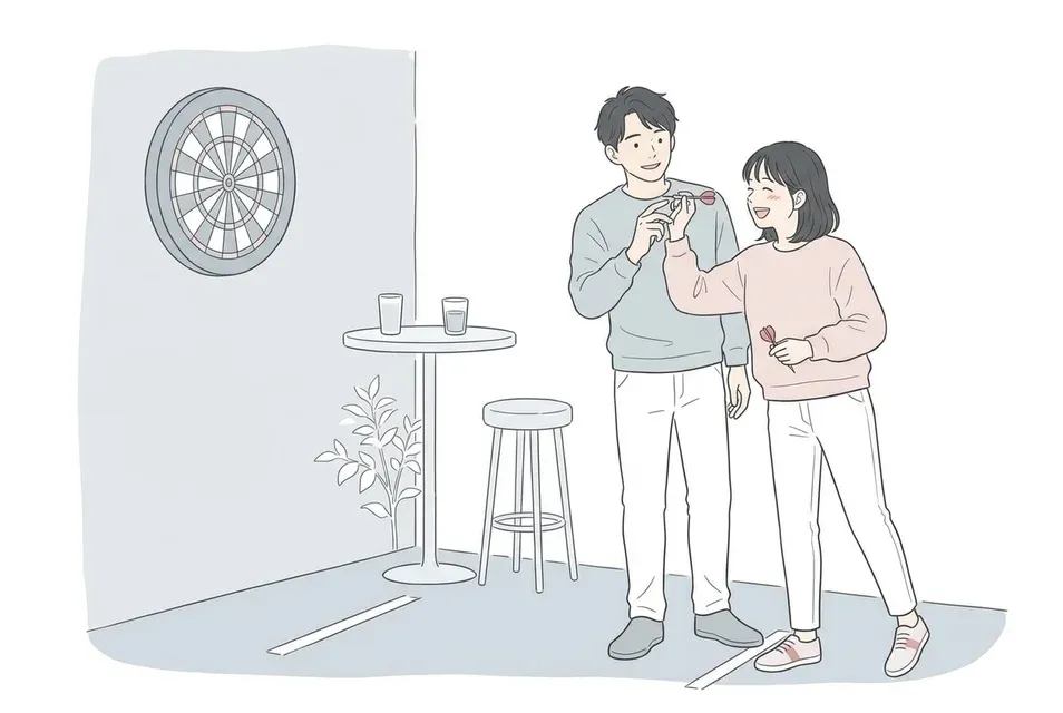 落ち着いたバーのダーツ台の前で、男性が女性にさりげなく投げ方を教えながら一緒に楽しむ様子